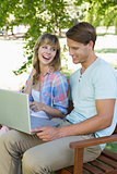Cute young couple sitting on park bench using laptop