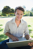 Stylish smiling man using his laptop in the park
