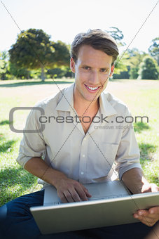 Stylish smiling man using his laptop in the park