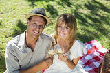 Cute couple drinking white wine on a picnic smiling at camera