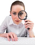 Businesswoman typing and looking through magnifying glass