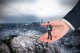 Composite image of serious businessman with hands on hips in large hand