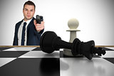 Composite image of serious businessman pointing a gun at chess piece