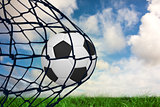 Composite image of football in back of the net
