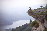 Young man sitting on edge of cliff and looking at river below