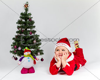 Dreaming baby boy dressed as Santa Claus lying next to Christmas