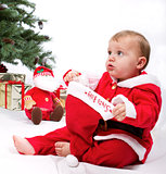 Santa Baby boy sitting next to Christmas tree.