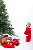 Fascinated Santa Baby boy standing next to Christmas tree.