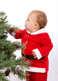 Santa Baby boy standing next to Christmas tree.