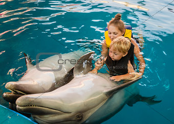 Mum with kid floats with dolphins in pool