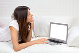 Young successful woman lying on a sofa with laptop paying bills 