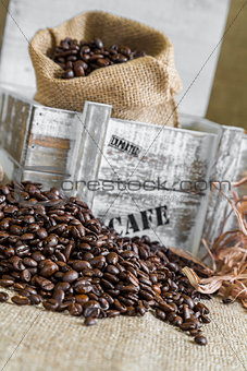 scattered coffee beans around wooden box with a burlap bag