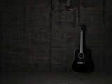 An wooden acoustic guitar is against a grunge textured wall. The room is dark with a spotlight for your copyspace. Use it for a music or concert concept.