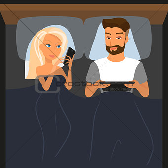 Happy couple using digital devices in bed at night.