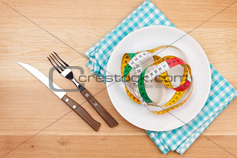 Plate with measure tape, knife and fork. Diet food on wooden tab