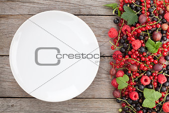 Fresh ripe berries and empty plate on wooden table