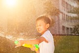 Cheerful little boy playing water guns in the park