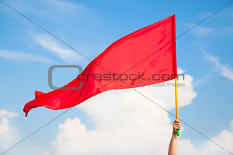 Hand waving a red flag with blue sky background 