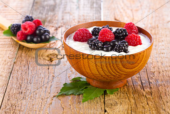 Yogurt with wild berries in wooden bowl