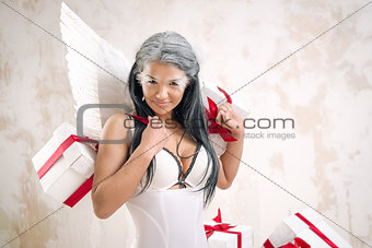 Young woman as angel with heap of gift boxes posing indoors