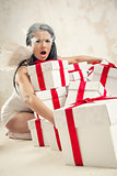 Beautiful young woman as angel with heap of gift boxes indoors