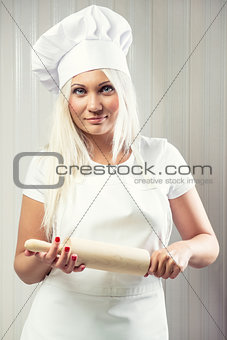 Woman holding rolling pin wearing uniform posing indoors