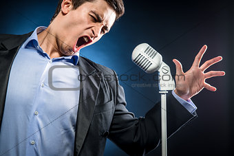 Man in elegant black jacket and blue shirt singing 