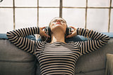 Young woman listening music in headphones while sitting on couch