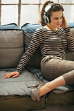 Young woman sitting on couch and listening music in headphones