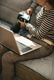 Closeup on young woman with laptop using modern dslr photo camer