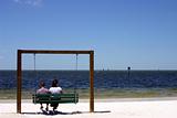 A couple sitting on a swing at the beach
