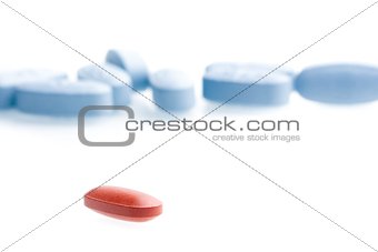 a single red medical pill in front of a lot of blue medical pills in laboratory
