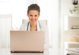 Happy doctor woman working on laptop in office