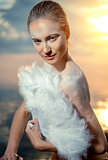 Woman with white feathers fan over sunset sky background 