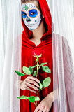 Day of the dead girl with sugar skull makeup holding red rose
