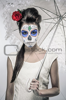 Day of the dead girl with sugar skull makeup holding lace umbrella