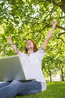 Pretty redhead using her laptop in the park and cheering