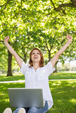 Pretty redhead using her laptop in the park and cheering