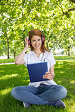 Pretty redhead using her tablet pc while listening to music in the park