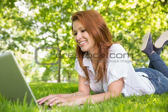 Smiling redhead using laptop in the park