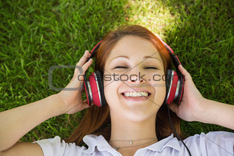 Pretty redhead lying on grass listening to music