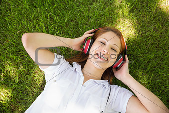 Pretty redhead lying on grass listening to music
