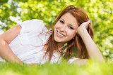 Pretty redhead lying on the grass smiling at camera