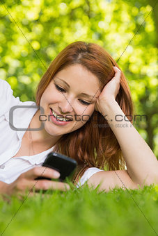 Pretty redhead lying on the grass sending a text