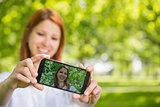 Pretty redhead taking a selfie on her phone in the park