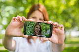 Pretty redhead taking a selfie on her phone in the park