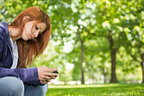 Pretty redhead relaxing in the park sending a text