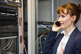 Pretty computer technician talking on phone beside open server