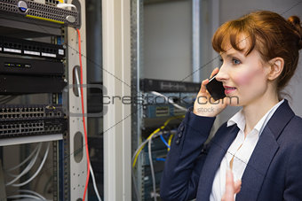 Pretty computer technician talking on phone beside open server
