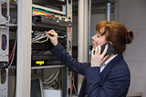 Pretty computer technician talking on phone while fixing server